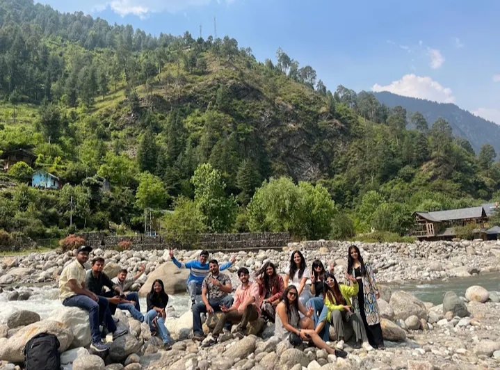 Group gathered on a rocky riverbank in the Tirthan Valley